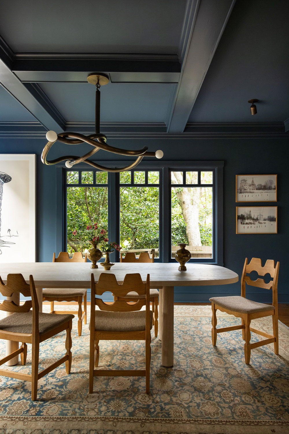 Dining room of Craftsman-style house in San Francisco's Presidio designed by Katie Troutman and featuring Henning Kjærnulf Razorblade chairs at a table atop an antique Persian Malayer rug under a chandelier by Paul Matter with a window flanked by a drawing by Claes Oldenburg and two pictures by Russian photographer Alexander Gronsky