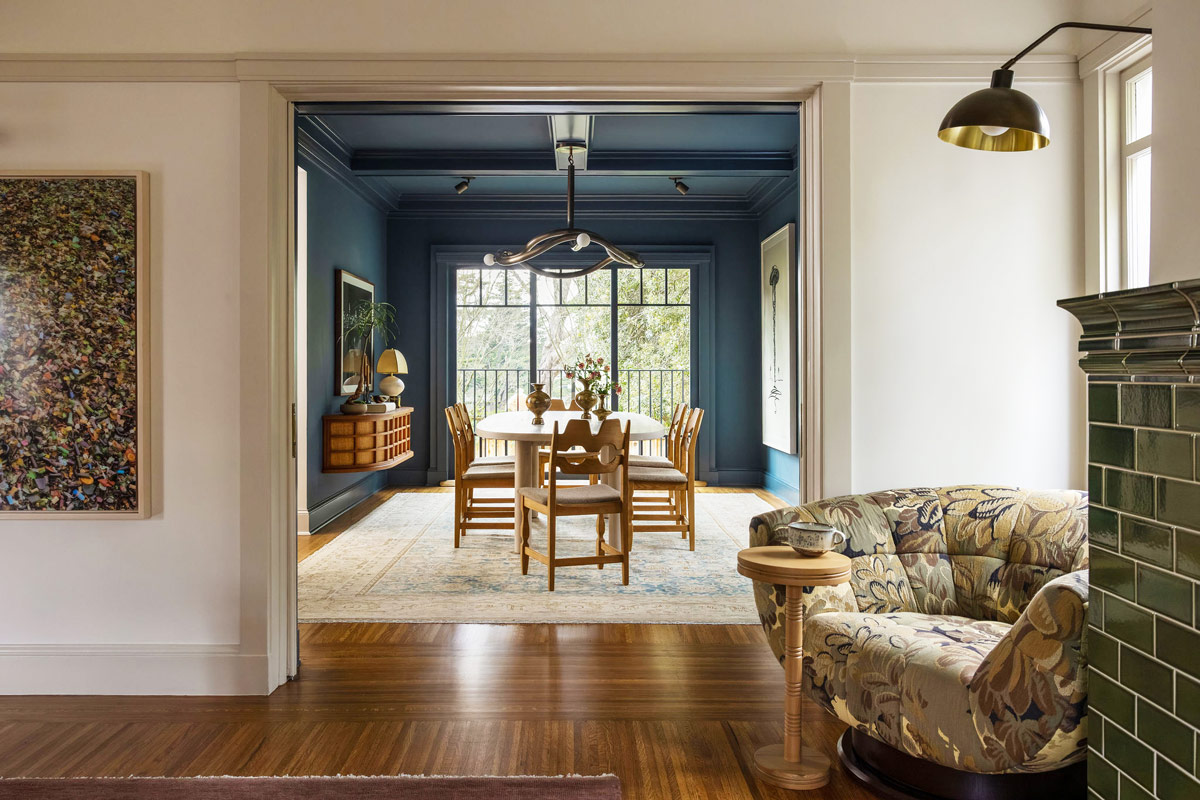 Living room with view through portal to dining room of Craftsman-style house in San Francisco's Presidio designed by Katie Troutman and featuring Adrian Pearsall armchair beside a green-tiled fireplace. Beyond, in dining room, Henning Kjærnulf’s Razorblade chairs sit at the table