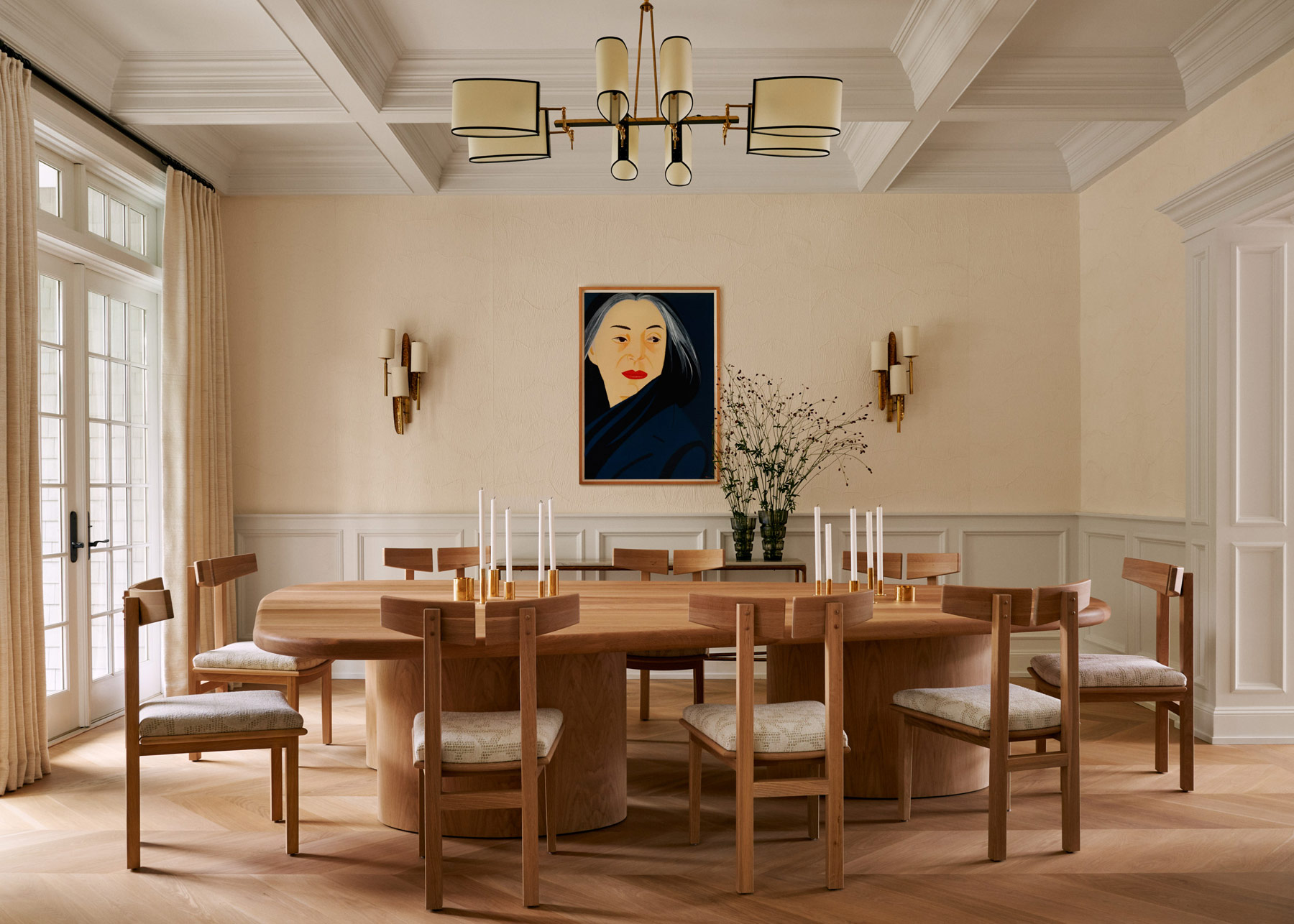 Alex Katz’s portrait of a woman bracketed by a pair of Maison Roche sconces from the 1960s, custom table and chairs and a 1950s Maison Lunel brass chandelier in the dining room of Southampton house with interiors by Janine Carendi MacMurray or Area Interior Design