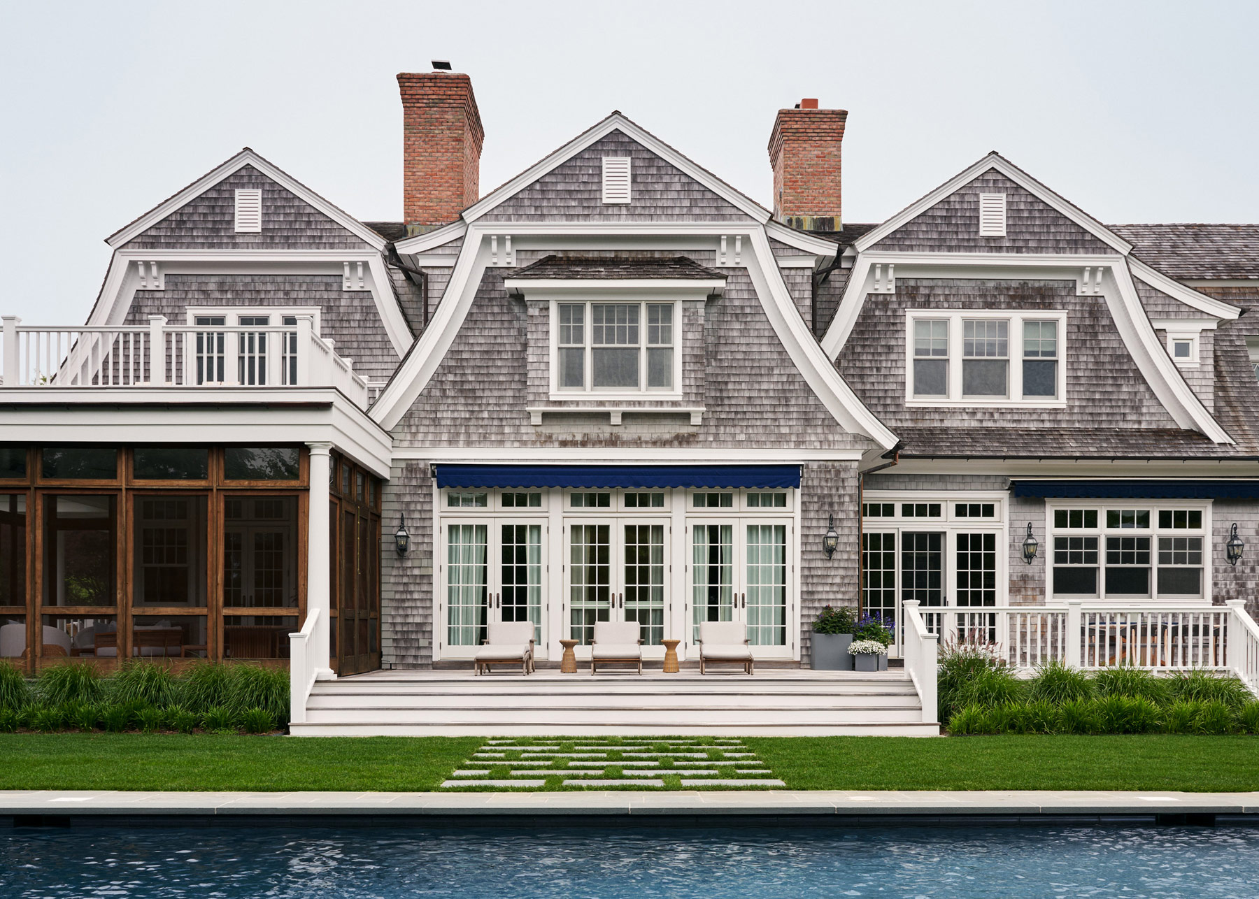Exterior of triple gabled gray shingled house in Southampton, New York with pool in front