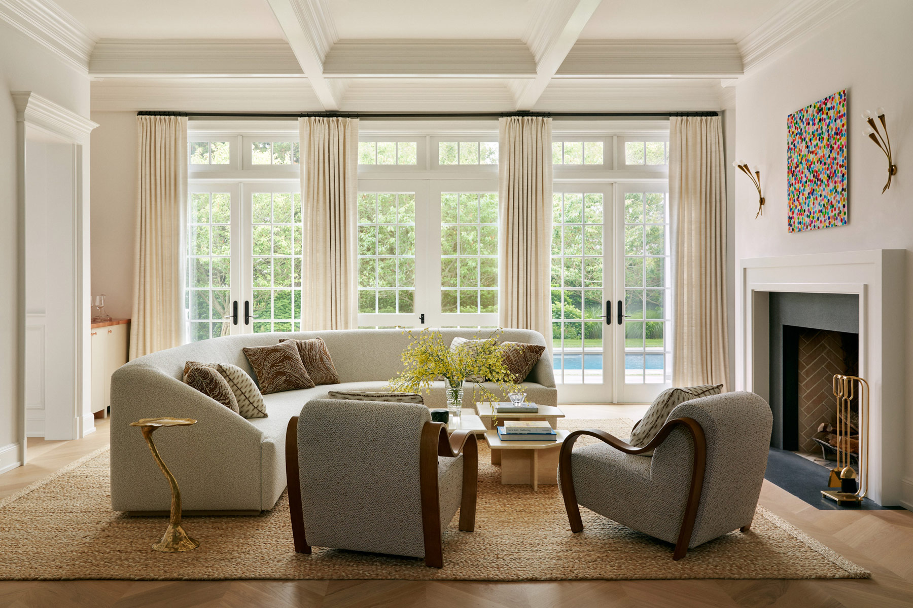 Custom L-shaped sofa, and chairs with curving wooden arms surrounded travertine coffee tables in the living room of Southampton house with interiors by Janine Carendi MacMurray or Area Interior Design