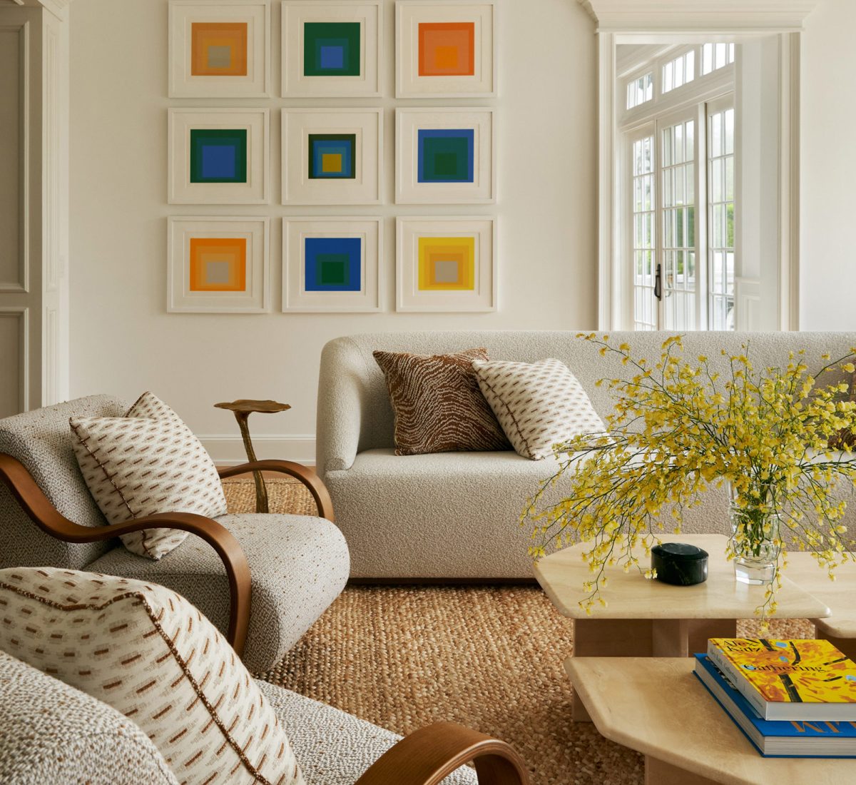 Josef Albers Homage to Square prints hung over a custom L-shaped sectional sofa and curving armchairs and travertine coffee tables in the living room of a Southampton house with interiors by Janine Carendi MacMurray of Area Interior design
