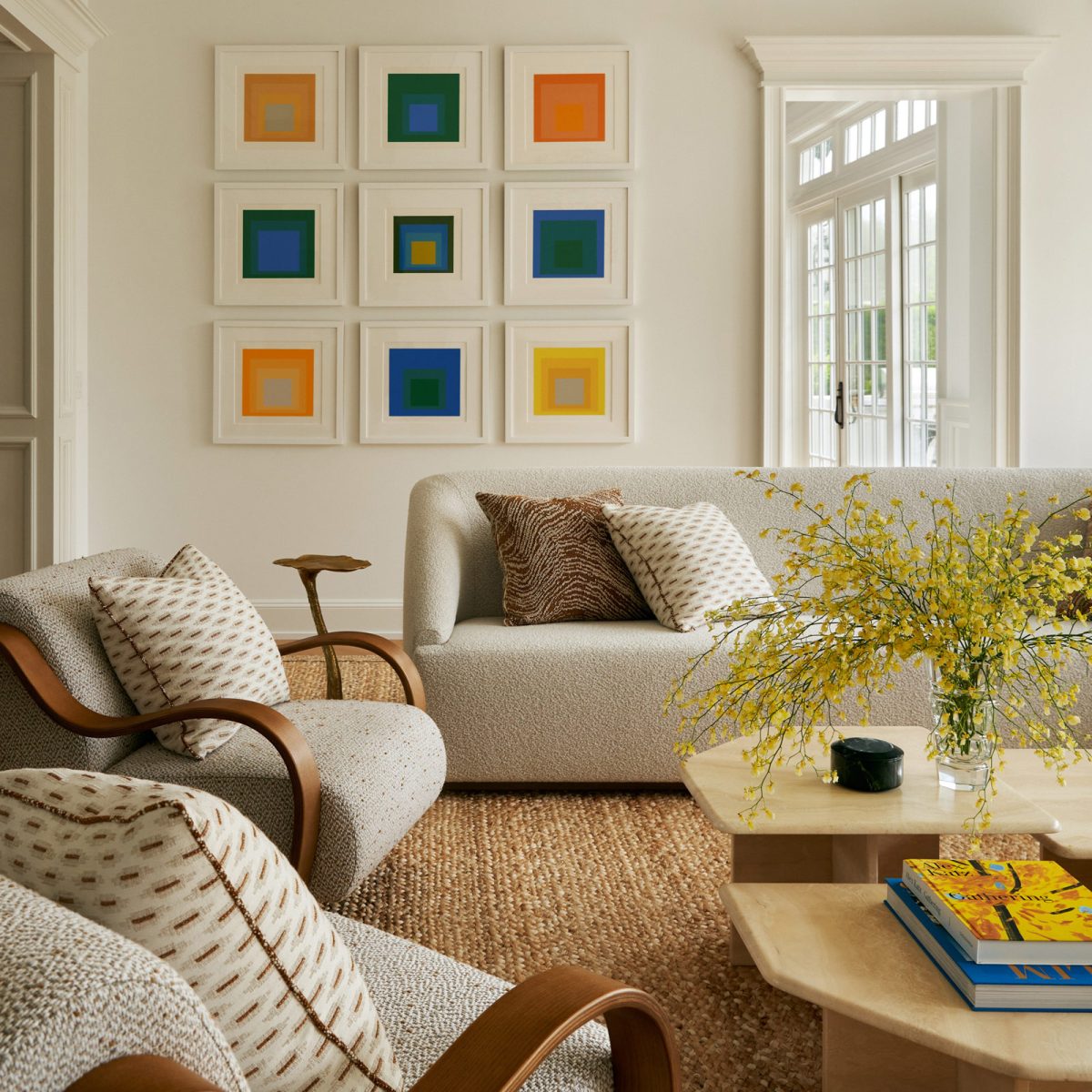 Josef Albers Homage to Square prints hung over a custom L-shaped sectional sofa and curving armchairs and travertine coffee tables in the living room of a Southampton house with interiors by Janine Carendi MacMurray of Area Interior design