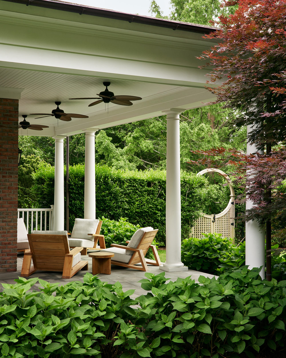 teak lounge chairs and table on covered porch of Southampton house with interiors by Janine Carendi MacMurray or Area Interior Design