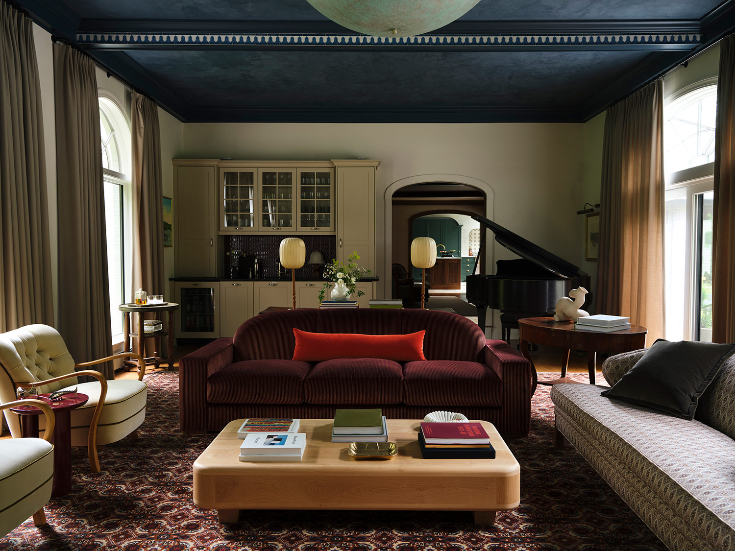 Custom patterned rugs, sofas cattycorner in Loro Piano fabric, Danish vintage armchairs, grand piano, and bar in the background in the great room of a New Hampshire house with interiors by designer Zoe Feldman