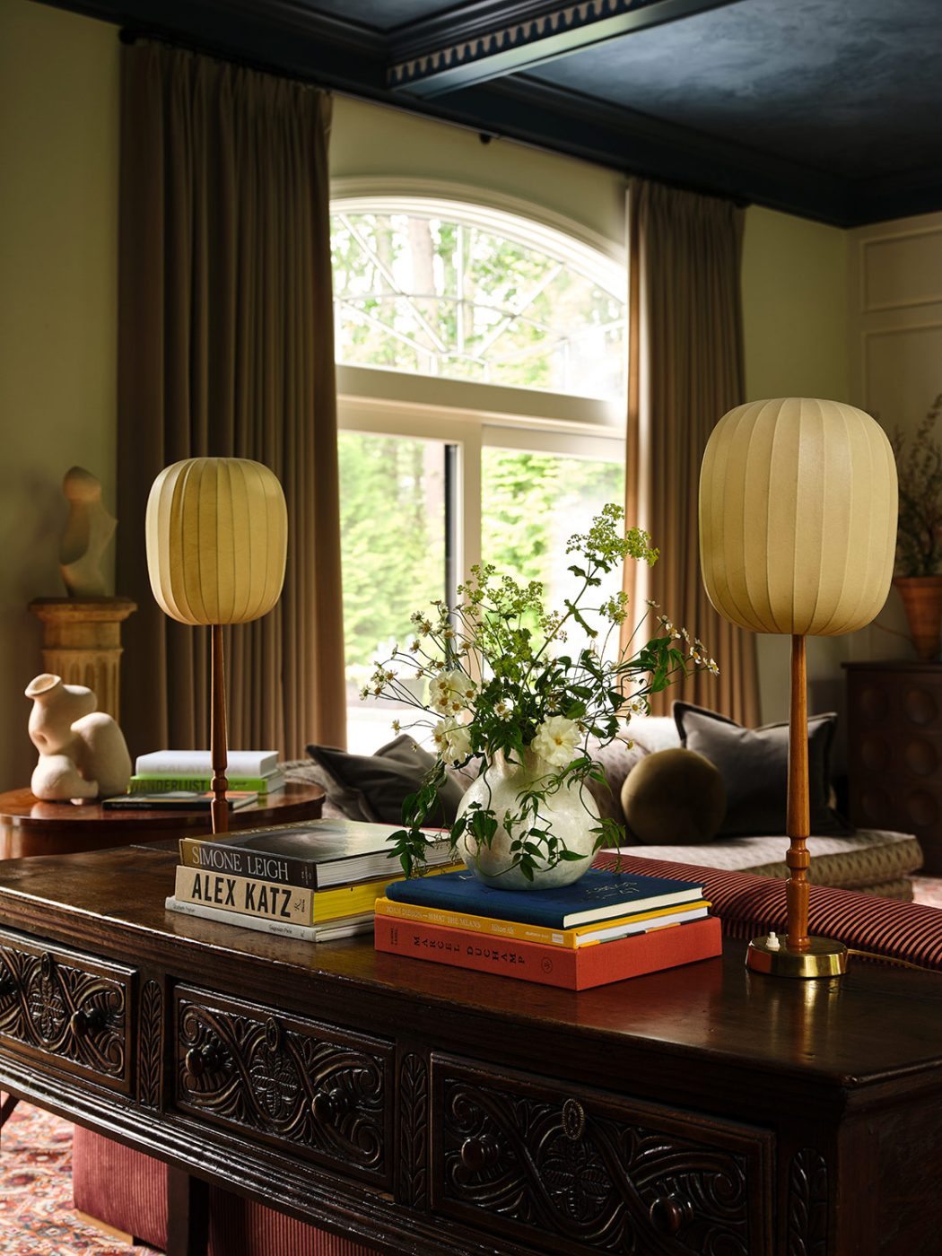 Vintage Hans Bergström table lamps from MDRN atop a carved consol table behind the sofa in the great room of a New Hampshire house with interiors by designer Zoe Feldman
