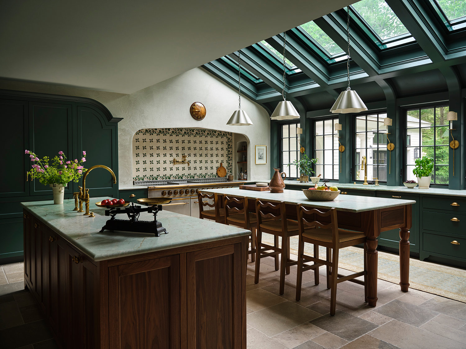 Skylit kitchen with green millwork and cabinets and wooden island and hightop table and painted tile backsplash behind range in the kitchen of a New Hampshire house with interiors by designer Zoe Feldman
