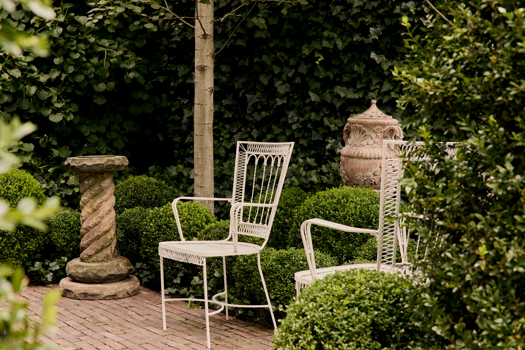 On offer by the gallery Galerie Green— a bronze sundial atop a carved-stone pedestal beside ribboned wrought-iron chairs in the garden of the Brooklyn garden design studio Harrison Green