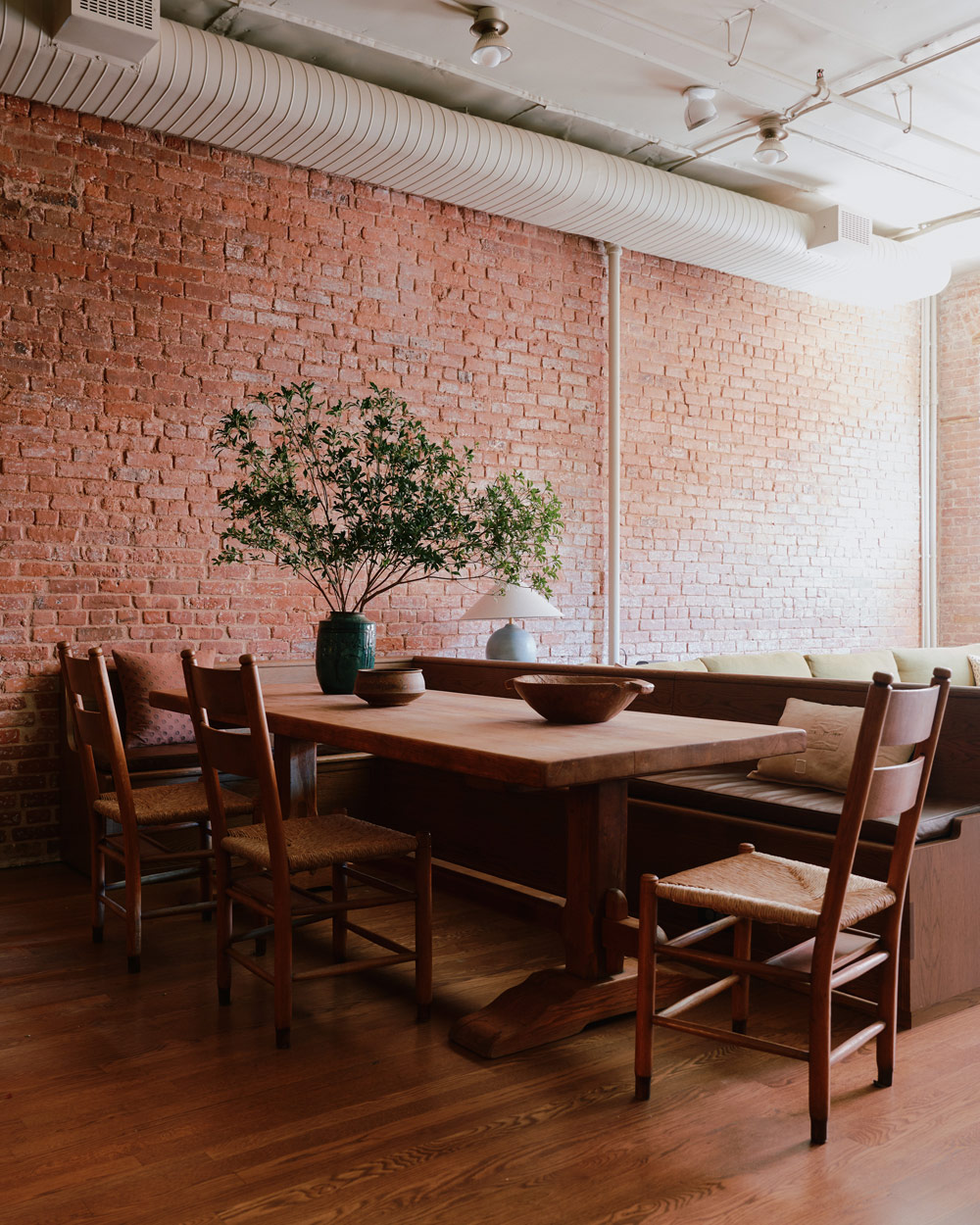 church pew-like banquette bench connected to back of sofa with trestle table and rush-seat ladder-back chairs in the dining area of a New York loft designed by Sarah Zames and Colin Stief, of the Brooklyn-based studio General Assembly