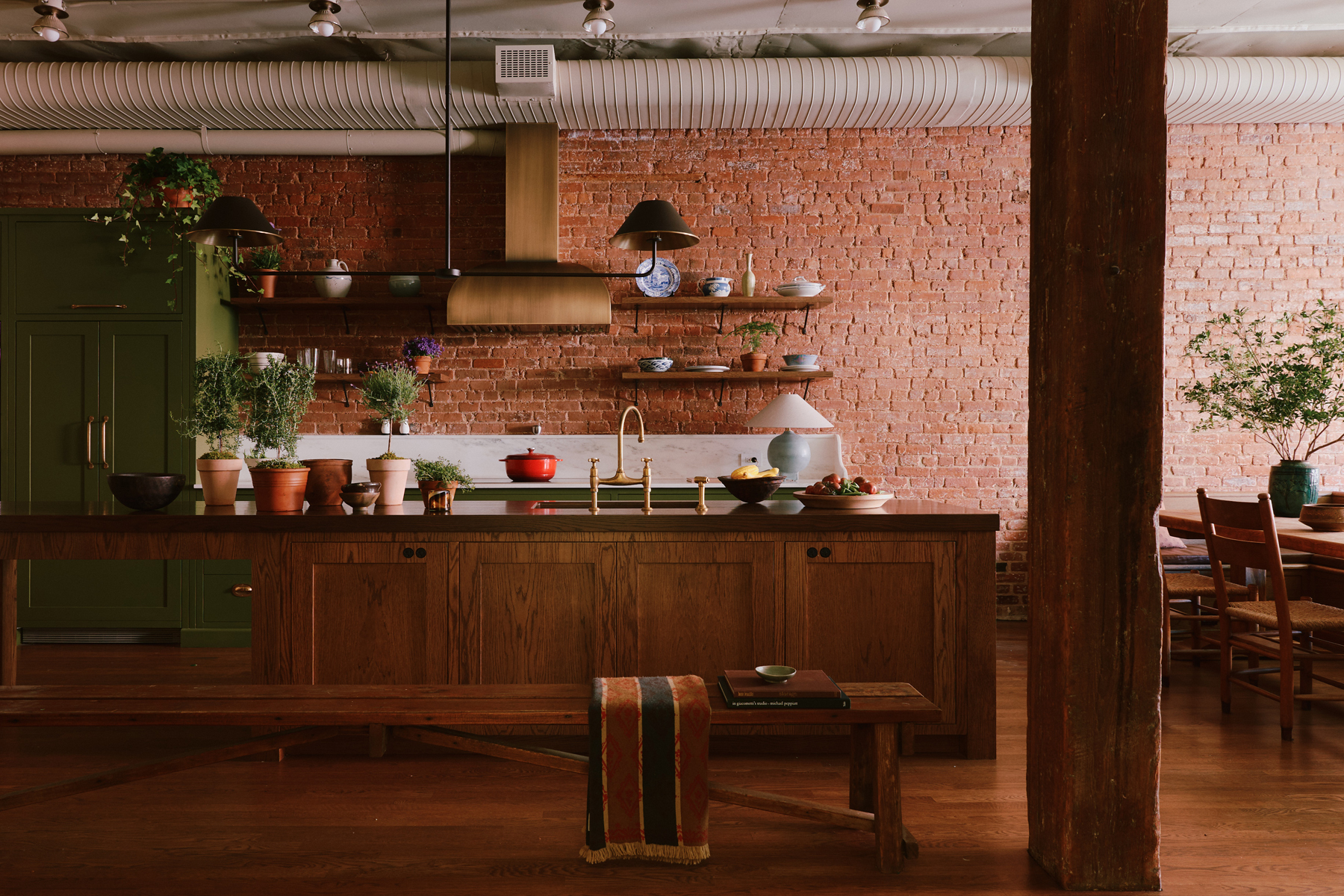Kitchen area fitted with a natural wood island and green painted marble topped cabinets along an exposed brick wall in a downtown New York loft designed by Sarah Zames and Colin Stief, of the Brooklyn-based studio General Assembly