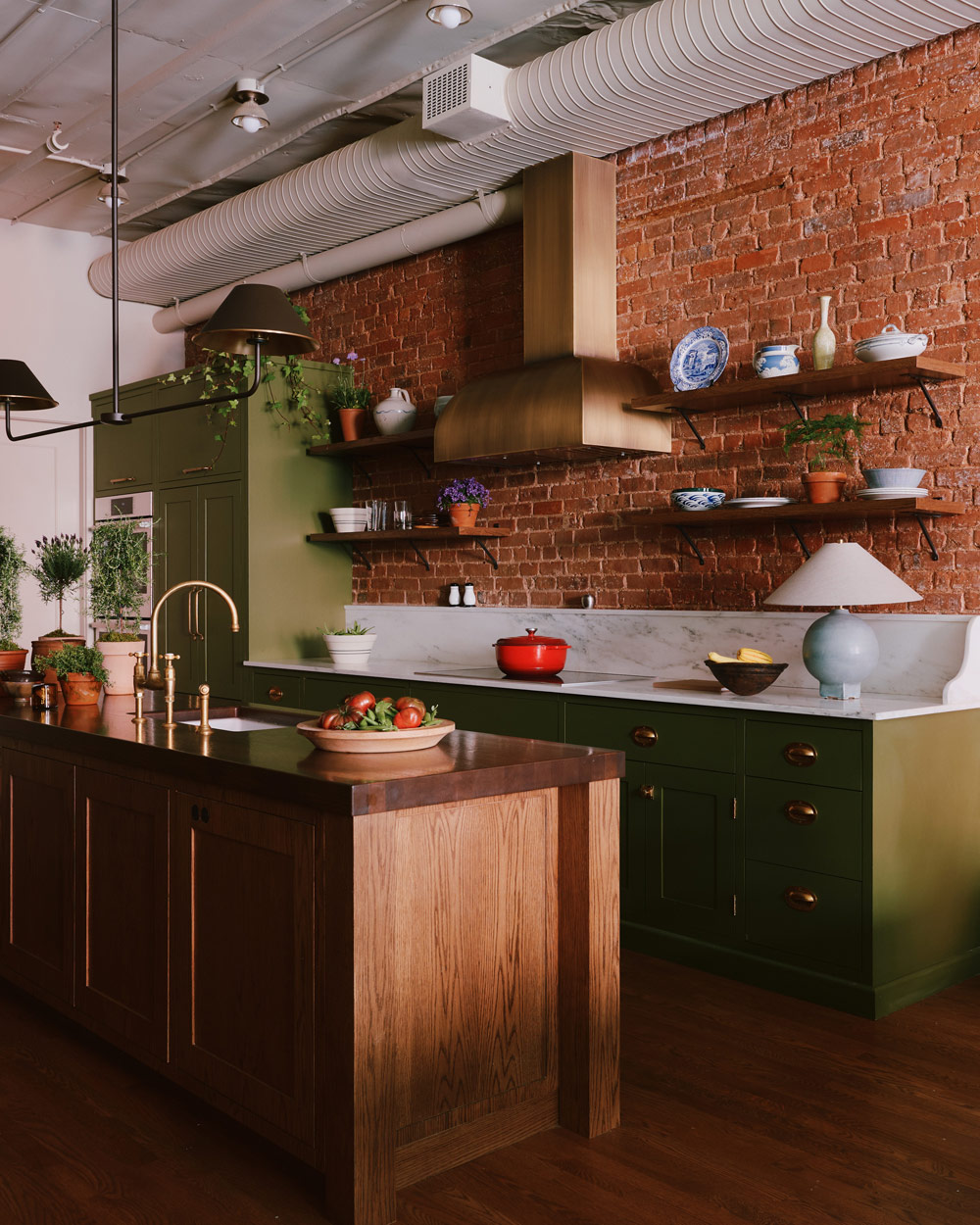 Kitchen area fitted with a natural wood island and green painted marble topped cabinets along an exposed brick wall in a downtown New York loft designed by Sarah Zames and Colin Stief, of the Brooklyn-based studio General Assembly