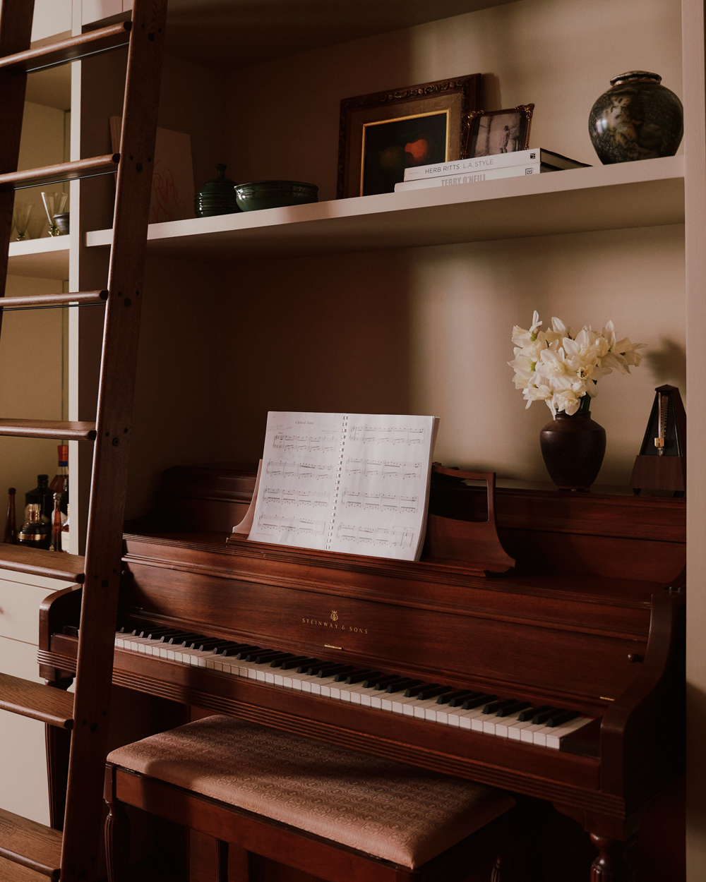 Upright wooden Steinway piano built into a wall of neutrally painted shelves filled with books and objects in a downtown New York loft designed by Sarah Zames and Colin Stief, of the Brooklyn-based studio General Assembly