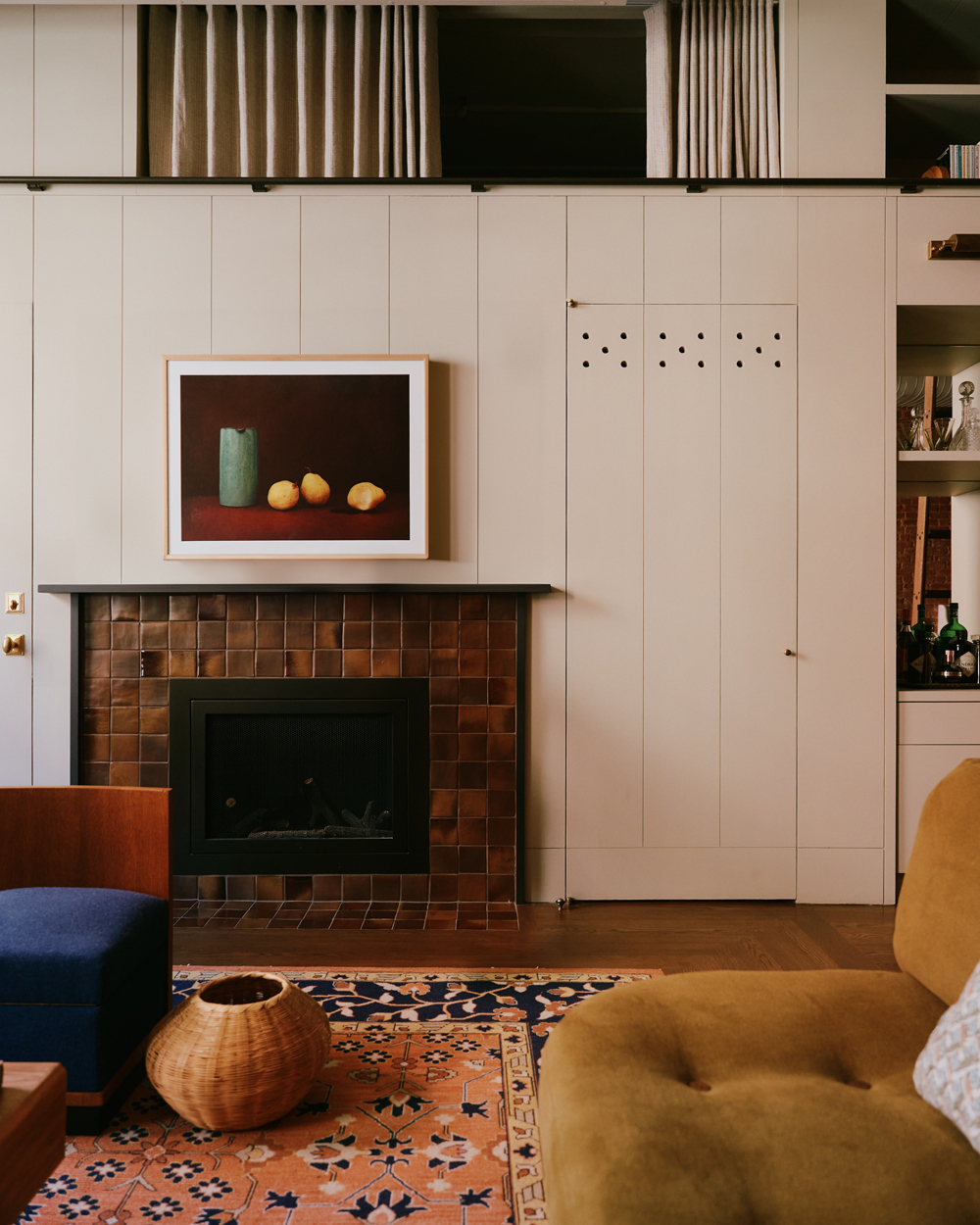 Fireplace with brown square tile surround and still life artwork above, against taupe wall panels in a downtown New York loft designed by Sarah Zames and Colin Stief, of the Brooklyn-based studio General Assembly