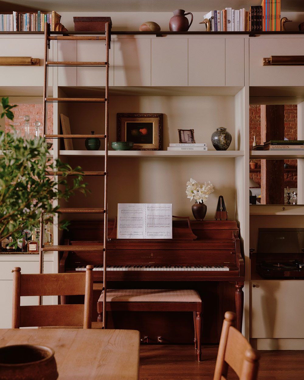 Upright wooden Steinway piano built into a wall of neutrally painted shelves filled with books and objects in a downtown New York loft designed by Sarah Zames and Colin Stief, of the Brooklyn-based studio General Assembly