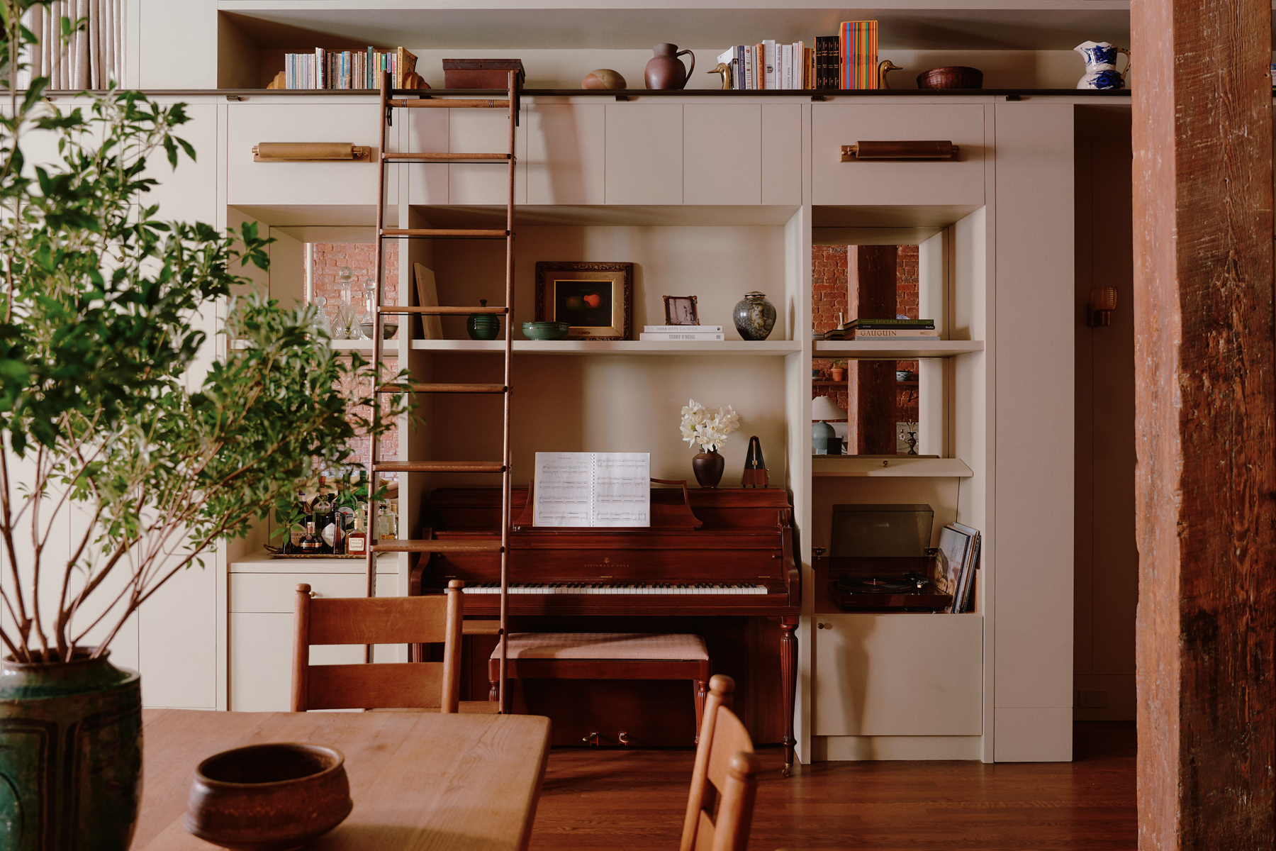 Upright wooden Steinway piano built into a wall of neutrally painted shelves filled with books and objects in a downtown New York loft designed by Sarah Zames and Colin Stief, of the Brooklyn-based studio General Assembly