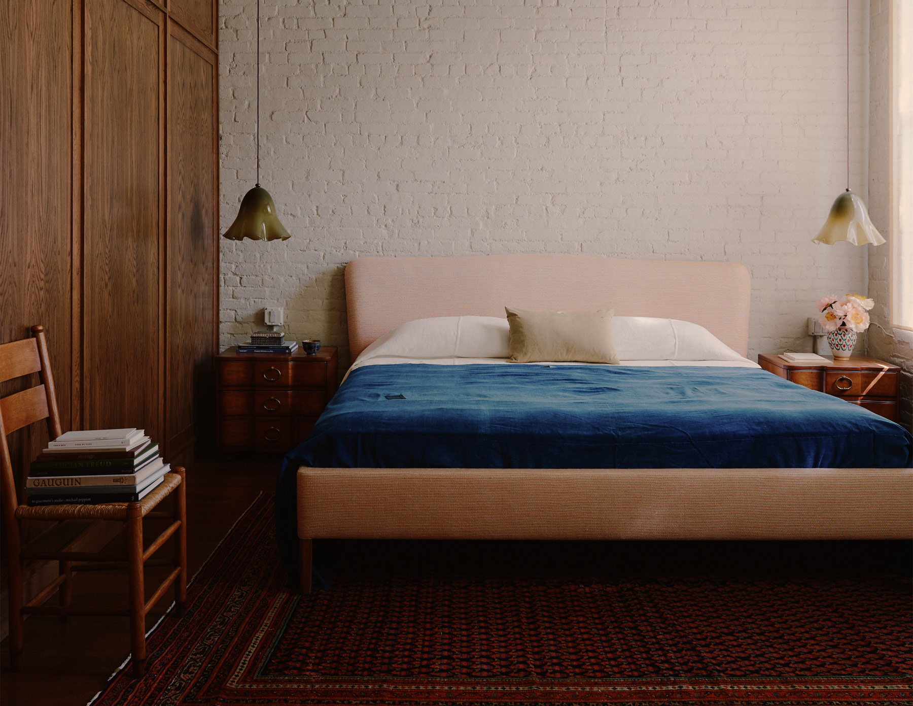 Pale pink upholstered bed with blue coverlet against white-painted brick wall in a downtown New York loft designed by Sarah Zames and Colin Stief, of the Brooklyn-based studio General Assembly