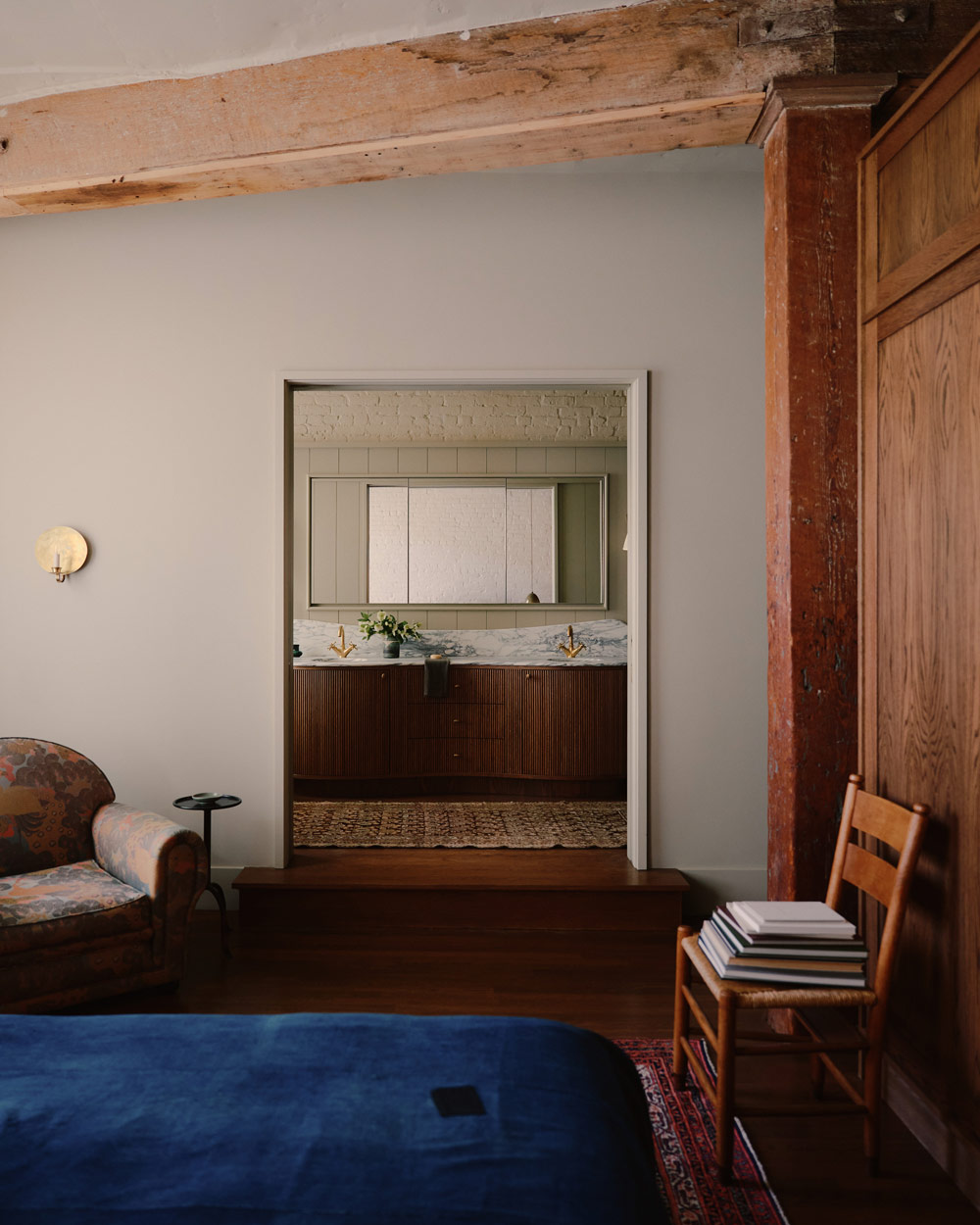 view from bed with blue coverlet in primary suite towards the bathroom with marble-topped double vanity in a downtown New York loft designed by Sarah Zames and Colin Stief, of the Brooklyn-based studio General Assembly