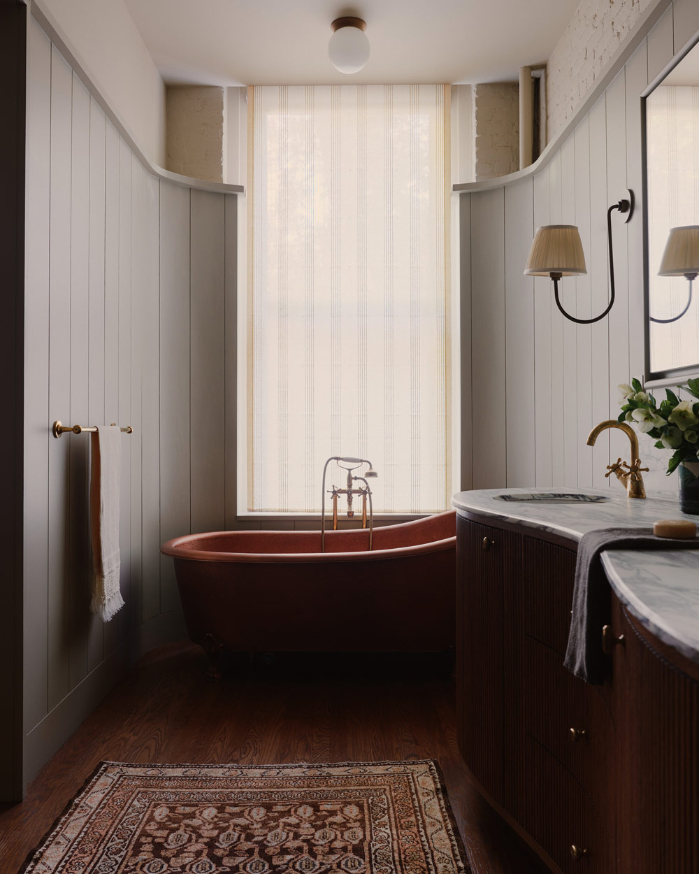 Primary bathroom with marble-topped double wooden vanity and copper slipper soaking tub in a downtown New York loft designed by Sarah Zames and Colin Stief, of the Brooklyn-based studio General Assembly