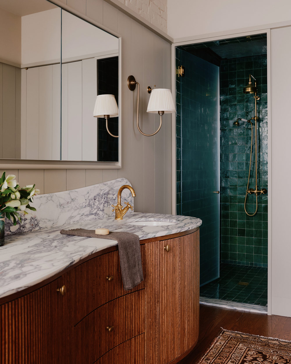 Primary bathroom with marble-topped double wooden vanity and stall shower with emerald-green square zellige tiles in a downtown New York loft designed by Sarah Zames and Colin Stief, of the Brooklyn-based studio General Assembly