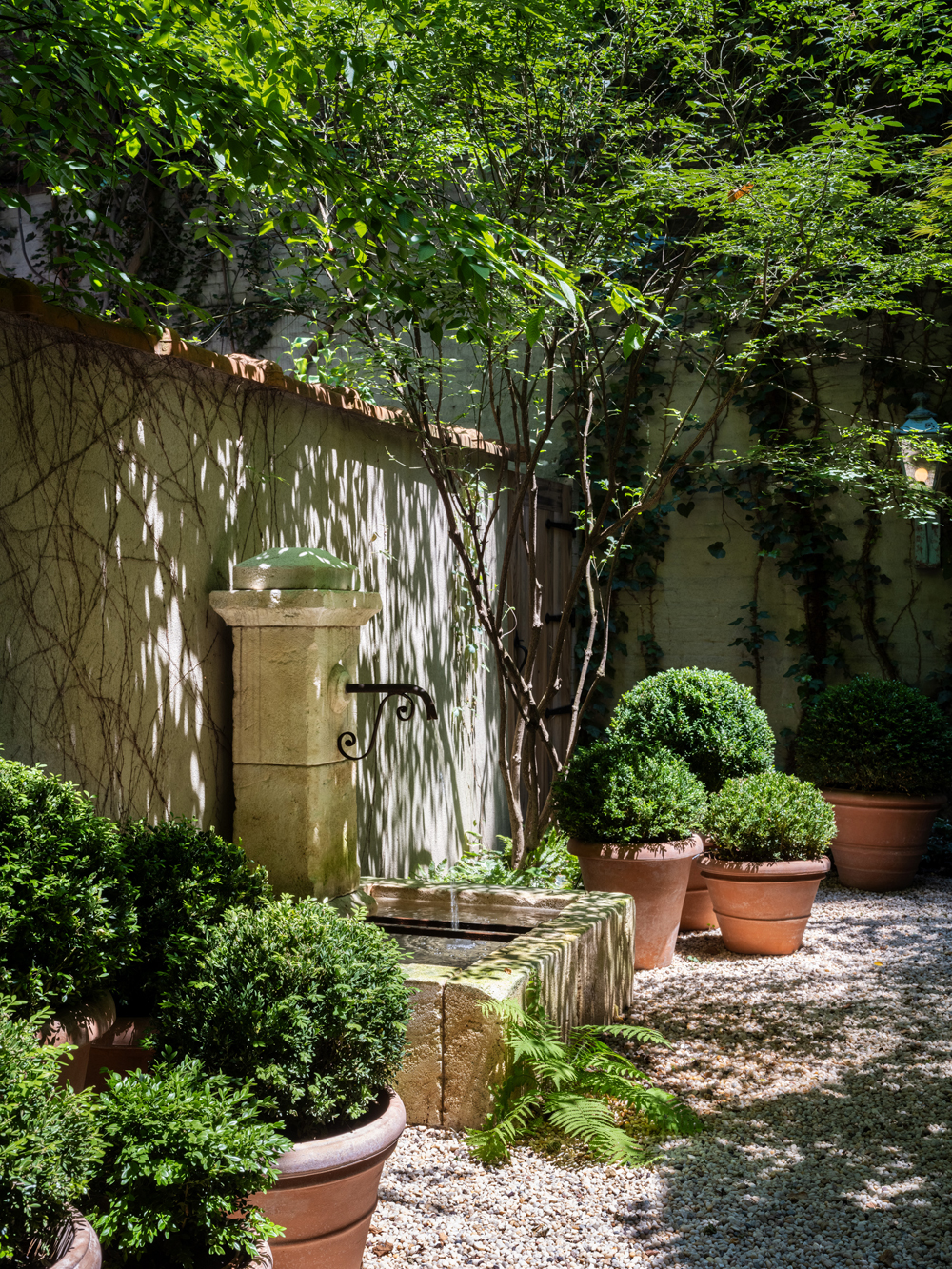 Residential courtyard garden in Manhattan's West Village designed by the Brooklyn studio Harrison Green and incorporating a French limestone vintage fountain set among boxwoods planted in terracotta pots