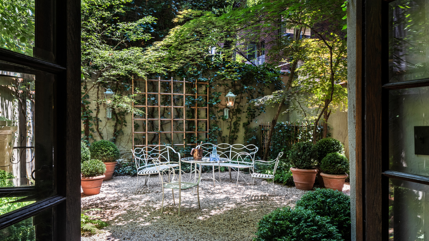 Residential courtyard garden in Manhattan's West Village designed by the Brooklyn studio Harrison Green and incorporating vintage white metal Leinfelder garden furniture among ferns, ground-cover plantings, boxwood in terracotta pots and vines climbing walls and trellises