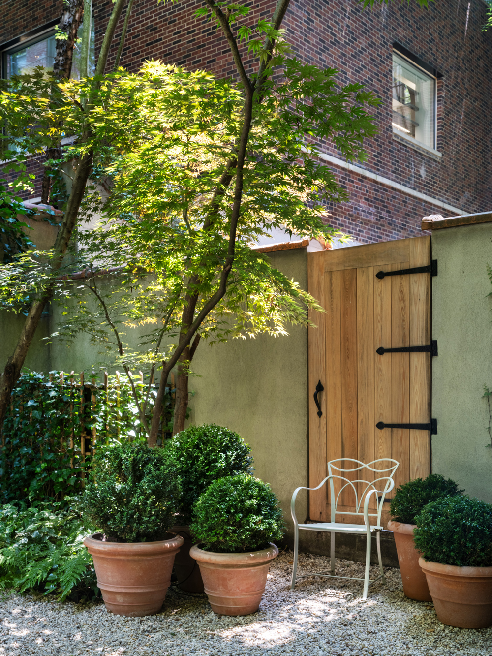 Residential courtyard garden in Manhattan's West Village designed by the Brooklyn studio Harrison Green and incorporating a vintage white metal Leinfelder garden chair set among boxwoods planted in terracotta pots