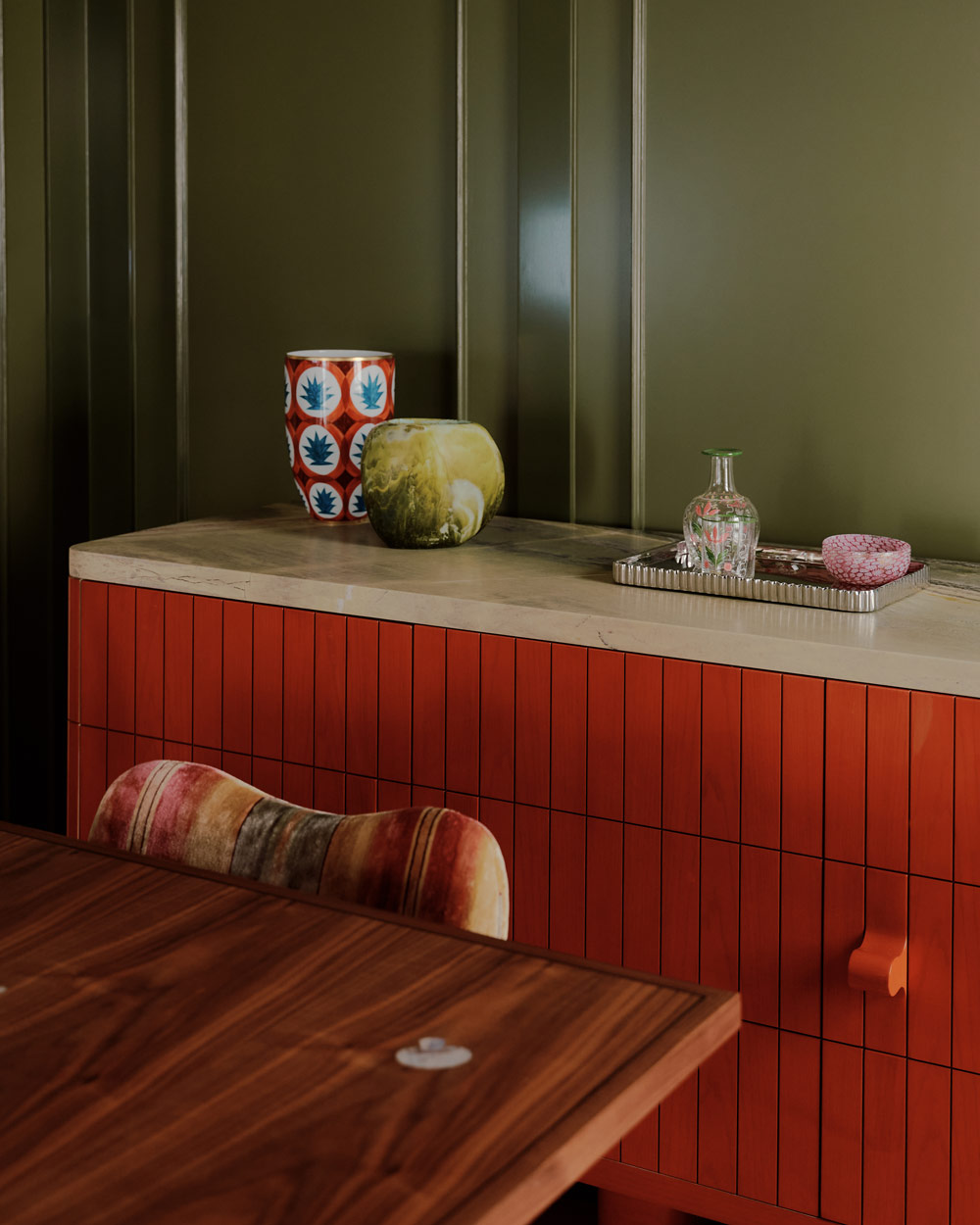 Red chest of drawers and wooded table and striped chair in front of green walls in the dining room of a duplex apartment on New York's Park Avenue designer by Bryan O'Sullivan