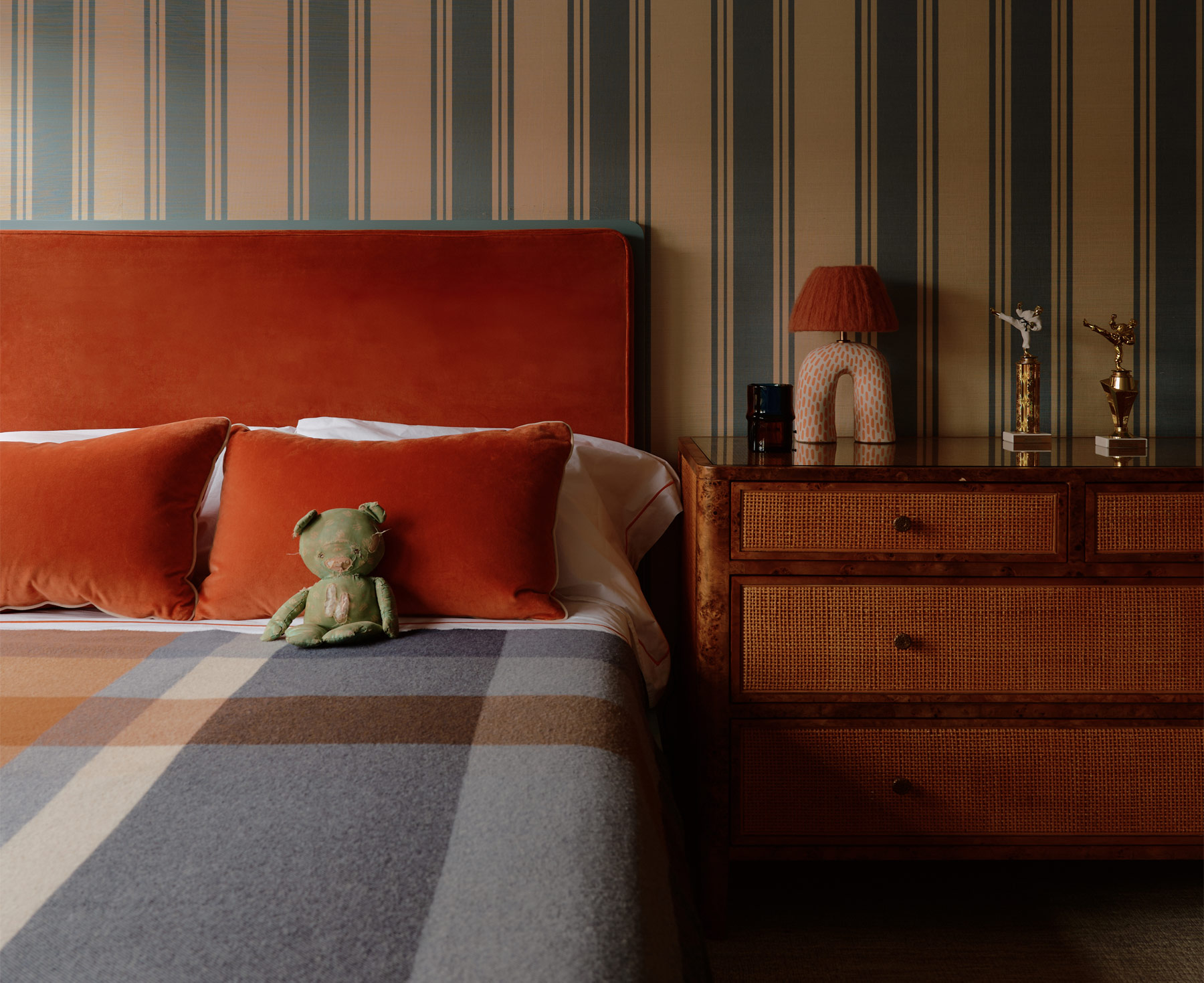 Cane-fronted burlwood chest of drawers and deep orange upholstered headboard against blue and white striped wallpaper in a son's room of a duplex apartment on New York's Park Avenue designer by Bryan O'Sullivan