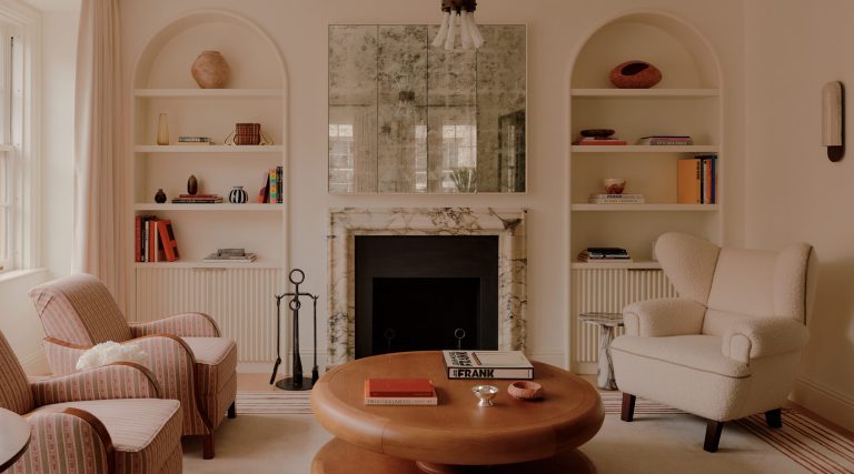 Living room with Swedish biedermeier arm chairs, leather-topped round coffee table, and boucle-covered wingback chair in front of a marble mantel under antiqued mirrors beside built-in shelves in a duplex apartment on New York's Park Avenue designer by Bryan O'Sullivan