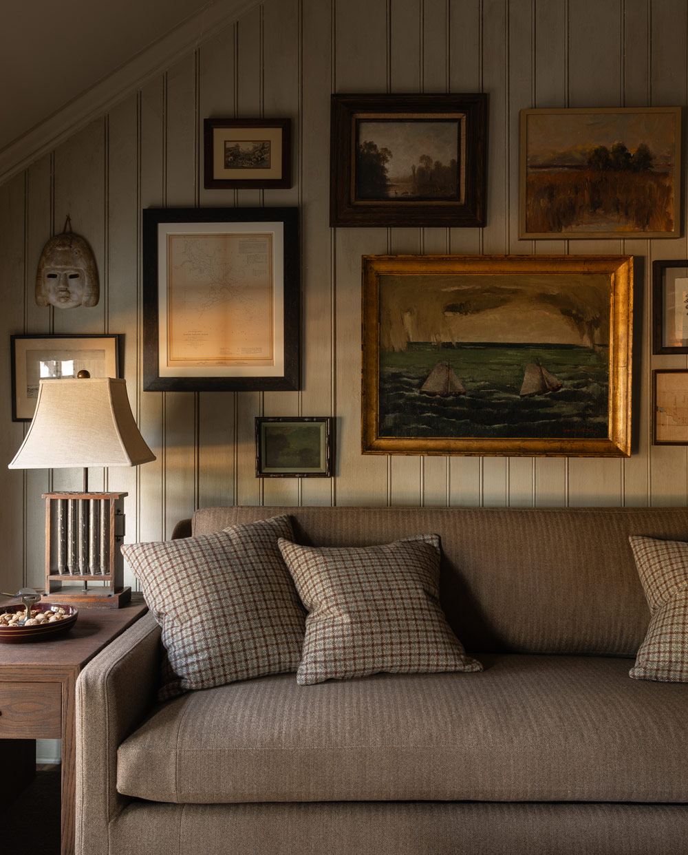 Seating area with sofa and art hung salon style over it in the primary bedroom of a former agrarian building on South Carolina's Edisto Island reimagined as a vacation home by interior designer Sean Anderson and architect Will Wingfield