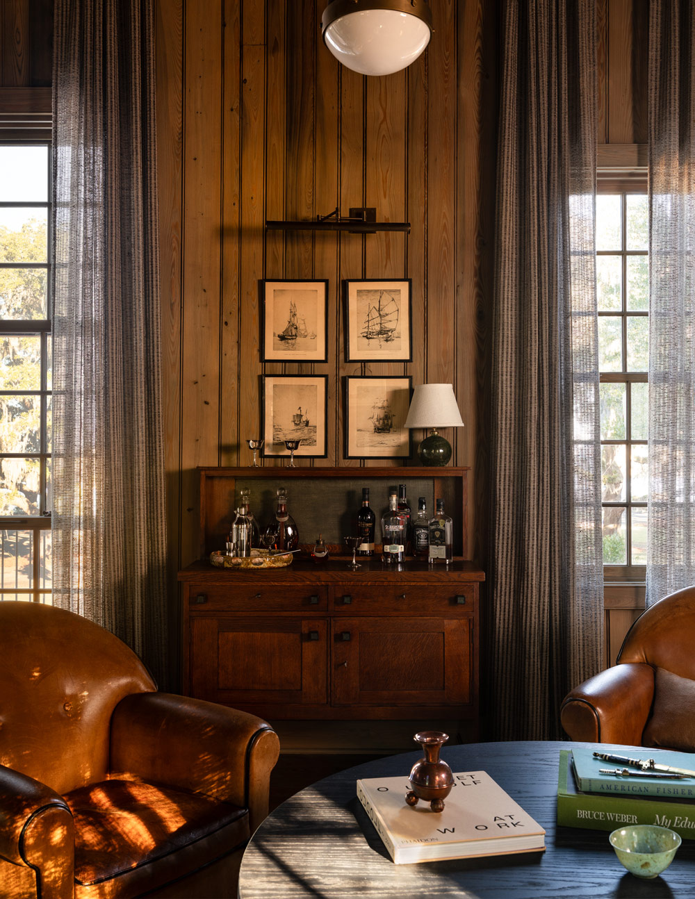 Bar area with leather club chairs in front in high-ceilinged barn-like great room of a former agrarian building on South Carolina's Edisto Island reimagined as a vacation home by interior designer Sean Anderson and architect Will Wingfield