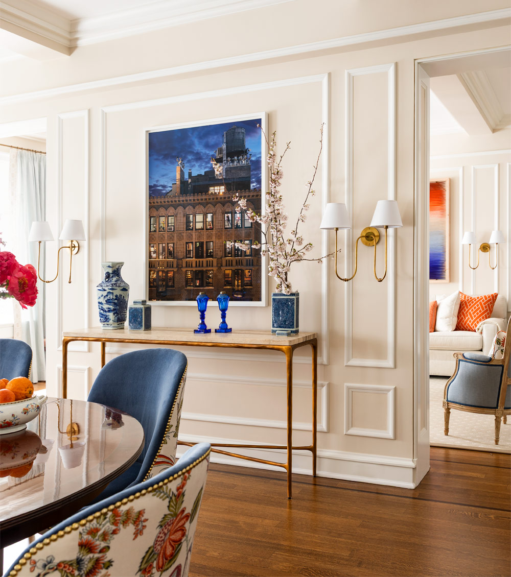 Dining room of Upper East Side New York pied-a-terre designed by Tom Stringer with console table and brightly colored contemporary art and botanical fabrics on dining chairs, set against largely neutral background