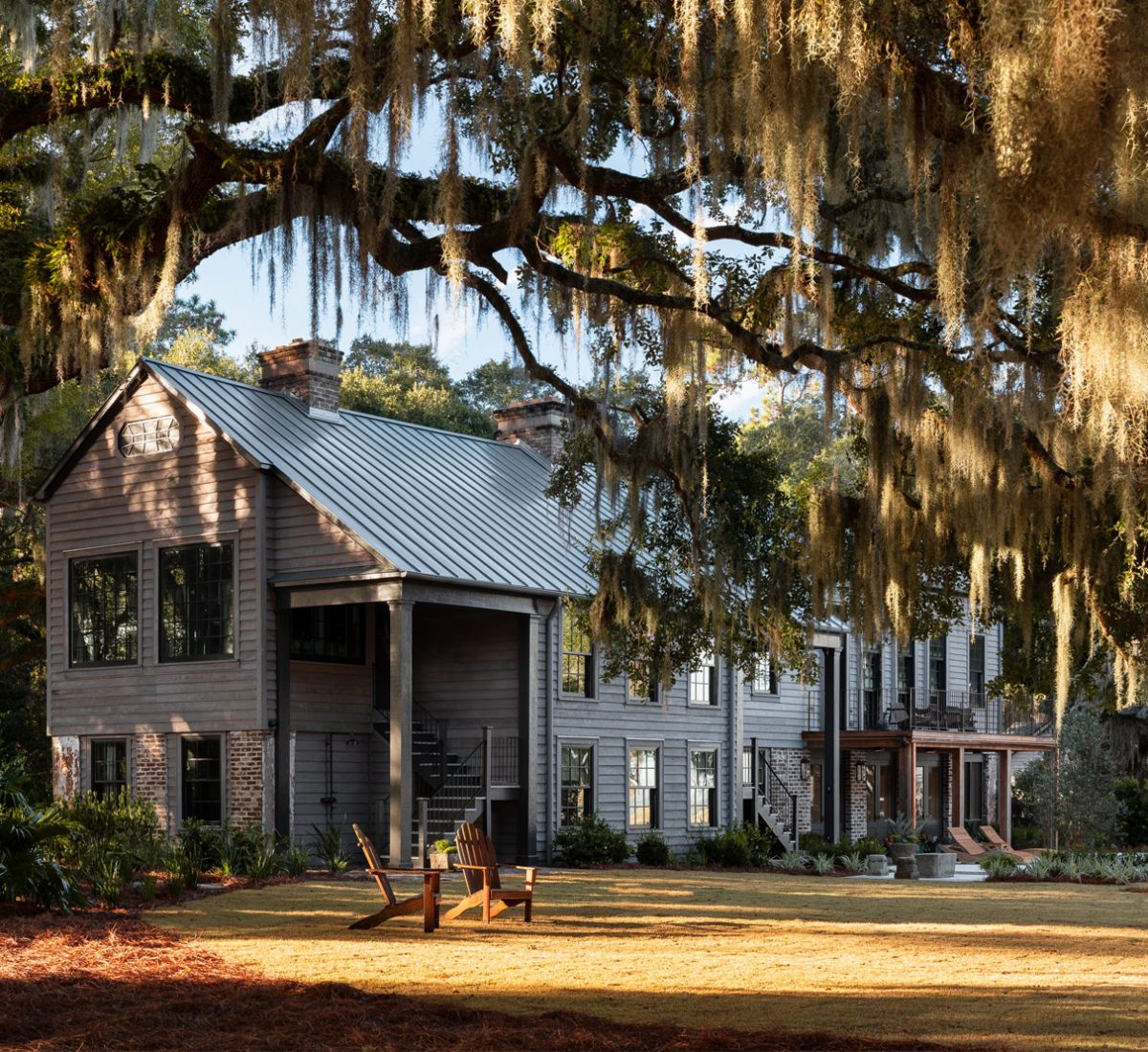 Exterior photo of a vacation house in a former barn-like agrarian building on South Carolina's Edisto Island reimagined by interior designer Sean Anderson and architect Will Wingfield. Landscape design by Glen R. Gardner. Live oak hung with spanish moss in forground