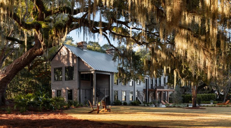 Exterior photo of a vacation house in a former barn-like agrarian building on South Carolina's Edisto Island reimagined by interior designer Sean Anderson and architect Will Wingfield. Landscape design by Glen R. Gardner. Live oak hung with spanish moss in forground